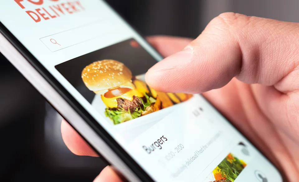 A person using a smartphone app to order a burger for delivery, illustrating the convenience of food delivery services in the gig economy.