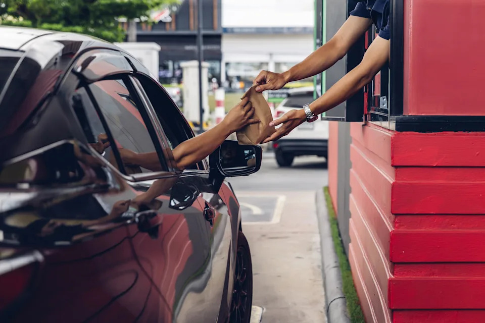 A picture of a car with an occupant receiving a paper bag of food from the window
