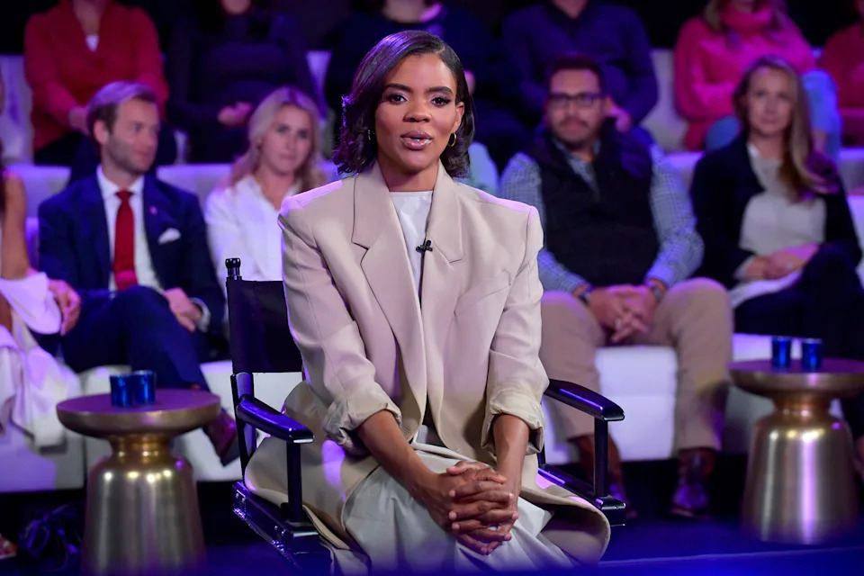 A man sits confidently in a suit on a TV show, surrounded by an audience
