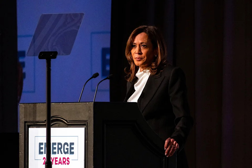 A man in a suit speaks from a scripted platform "REPRESENT," delivering a speech via a visual teleprompter