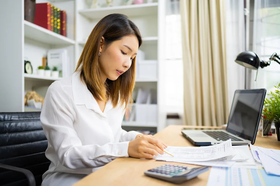 Man sitting at desk, concentrating on paperwork, with laptop and calculator near home office.