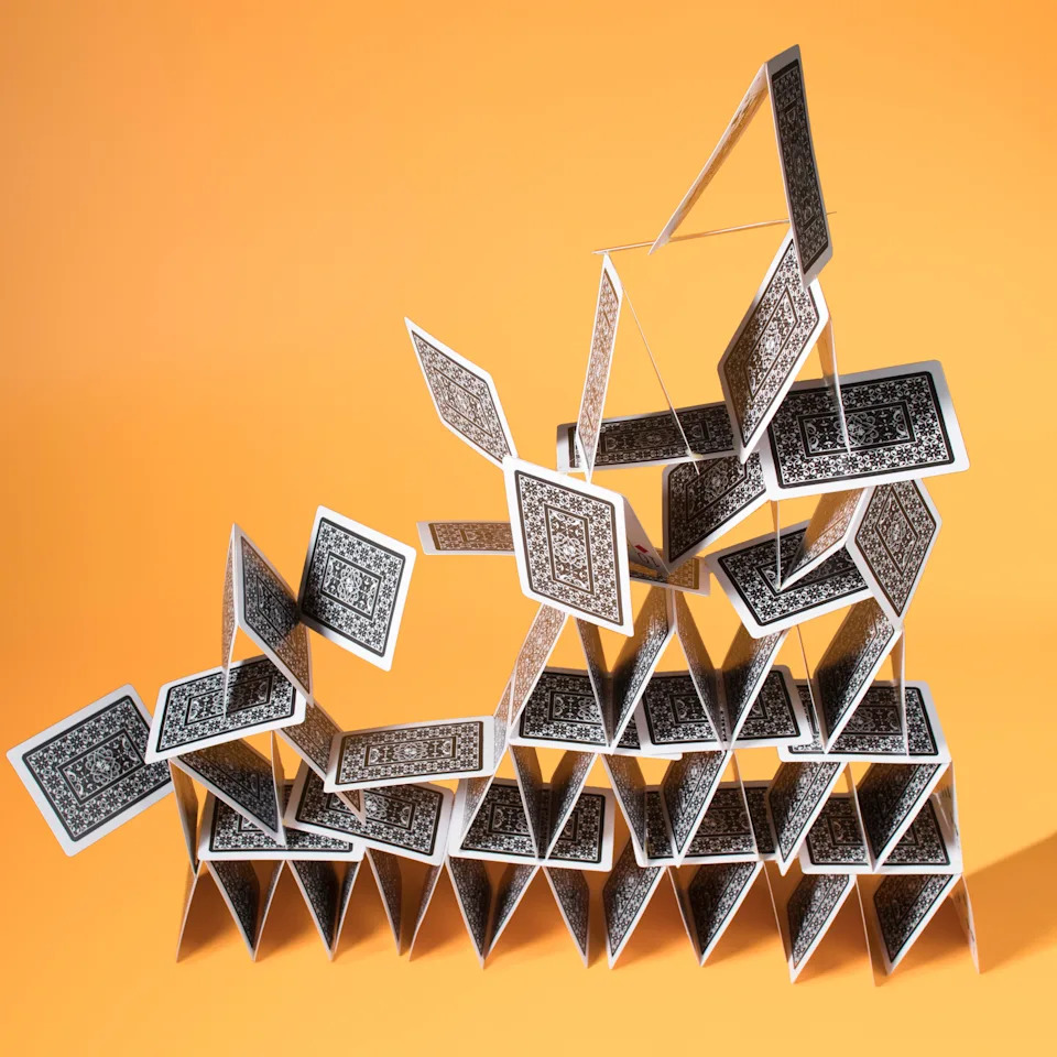 An elaborately designed house of cards against a plain exterior, with an intricate, multi-story building with upright standing cards.